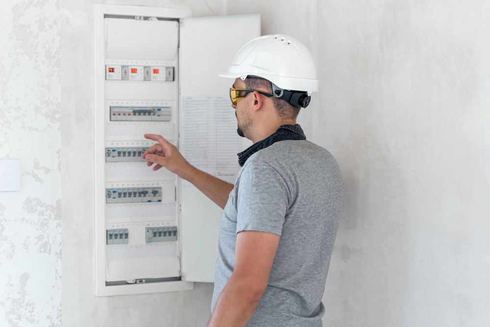 Električar sa zaštitnom kacigom i naočarima proverava FID sklopke i automatske osigurače u otvorenoj razvodnoj tabli